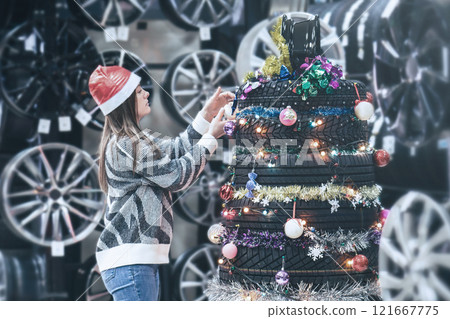 Woman decorates stack of tires as festive Christmas tree in city using colorful ornaments Woman decorates stack of tires as festive Christmas tree in city using colorful ornaments 121667775