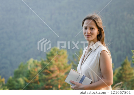 A woman holds a notebook in a serene nature setting, projecting professionalism and focus A woman holds a notebook in a serene nature setting, projecting professionalism and focus 121667801