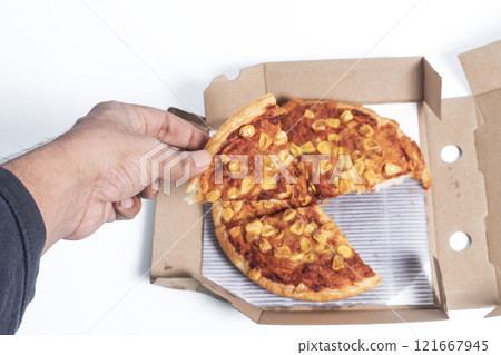 Hand holding a pizza slice from a box with corn topping 121667945