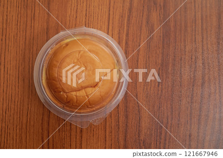 Round butter bun in plastic packaging on a wooden table surface, top view 121667946