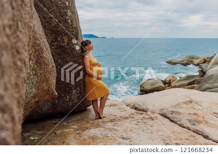Pregnant happy woman in yellow dress posing at ocean coastline 121668234