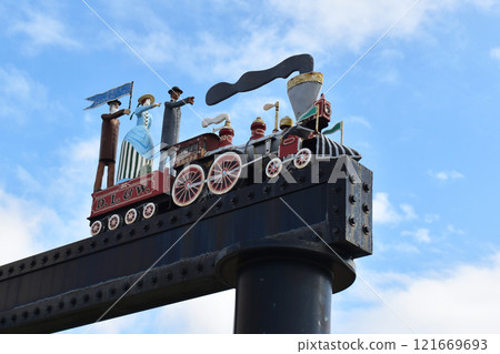 old toy steam locomotive against the blue sky, cute vintage sculpture of a train with people at the city railway station 121669693