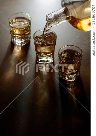 Whiskey pour from a bottle into a small glasses. 121669704