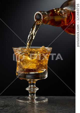 Strong alcoholic drink is poured into a glass with ice. 121669716