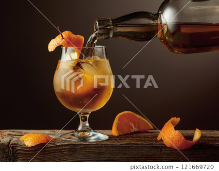 Old Fashioned cocktail with ice and orange peel on a old wooden table. 121669720