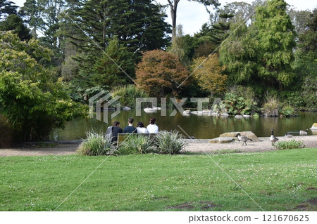 Unidentified people sitting on a bench in the city park. People walking in park Unidentified people sitting on a bench in the city park. People walking in park 121670625