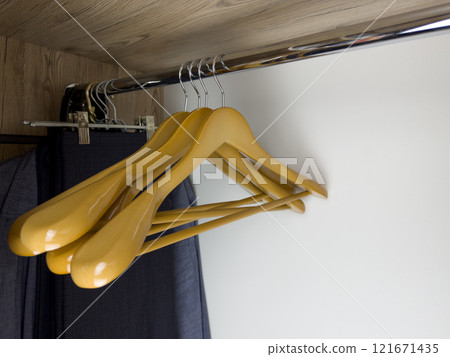 Set of convenient light wood hangers hanging on beam inside clothes closet at home, hangers in closet without clothes, storing clean clothes at home Set of convenient light wood hangers hanging on beam inside clothes closet at home, hangers in closet without clothes, storing clean clothes at home 121671435