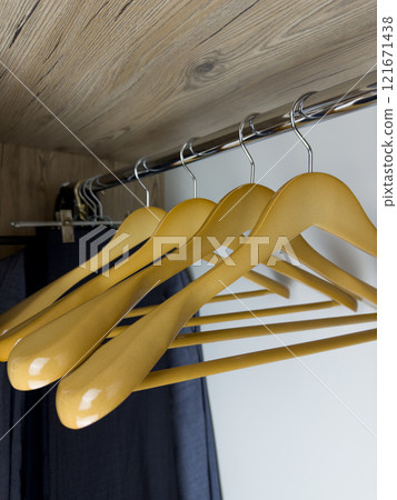 Close up photo of wooden clothes hangers inside clothes closet, empty hangers for easy storage of clean clothes at home inside wardrobe, durable wooden hangers on beam in wardrobe 121671438