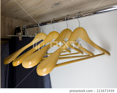 Empty light wood hangers hang on beam inside closet, place to store new clothes on hangers with crossbar for storage of pants. Empty space for clothes in wardrobe at home. Clothing storage device 121671439