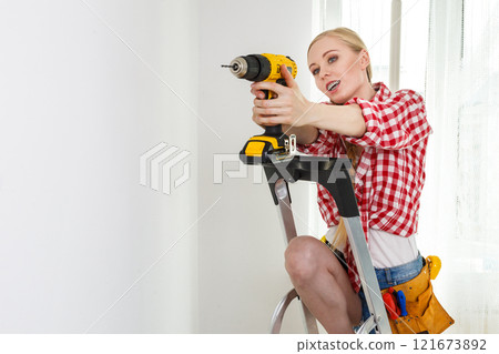 Woman using drill on ladder 121673892