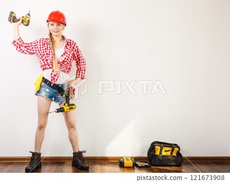 Woman wearing helmet, toolbelt about to drill wall Woman wearing helmet, toolbelt about to drill wall 121673908