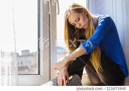 Sad depressed teen girl sitting on window sill 121673940