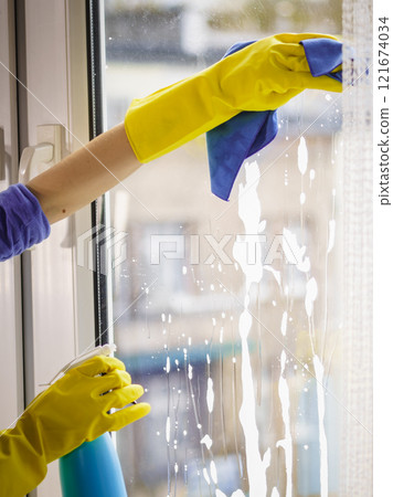 Gloved hand cleaning window rag and spray 121674034