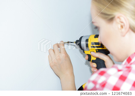 Woman drilling in wall Woman drilling in wall 121674083