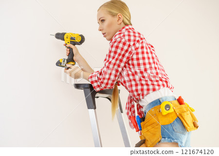 Woman on ladder using drill Woman on ladder using drill 121674120