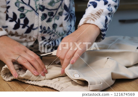 A woman is examining classic beige trousers. She is demonstrating the inside of the pants.  121674569