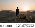 Woman stands alone on the high rock during sunset and looking at setting sun in distance 121675332