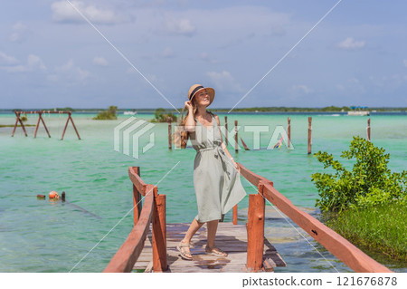 Female tourist in a turquoise dress standing on a wooden pier over the turquoise waters of Bacalar Lake, Mexico. Peaceful tropical travel destination concept Female tourist in a turquoise dress standing on a wooden pier over the turquoise waters of Bacalar Lake, Mexico. Peaceful tropical travel destination concept 121676878