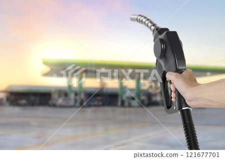 Holding a fuel nozzle against with gas station blurred background Holding a fuel nozzle against with gas station blurred background 121677701