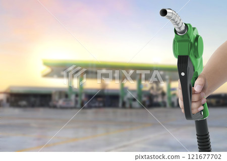 Holding a fuel nozzle against with gas station blurred background Holding a fuel nozzle against with gas station blurred background 121677702