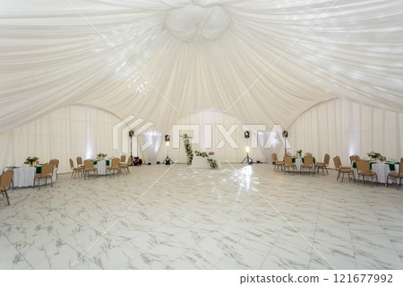 Close up of wine glasses, silver tableware and green napkins on round tables covered with white tablecloth. 121677992