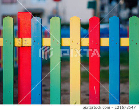 The colorful painted wooden boards on the fence around a playground are illuminated by the rays of the setting sun. Pula, Croatia - January 3, 2025 The colorful painted wooden boards on the fence around a playground are illuminated by the rays of the setting sun. Pula, Croatia - January 3, 2025 121678547
