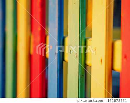 The colorful painted wooden boards on the fence around a playground are illuminated by the rays of the setting sun. Pula, Croatia - January 3, 2025 121678551