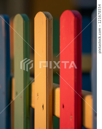 The colorful painted wooden boards on the fence around a playground are illuminated by the rays of the setting sun. Pula, Croatia - January 3, 2025 The colorful painted wooden boards on the fence around a playground are illuminated by the rays of the setting sun. Pula, Croatia - January 3, 2025 121678554