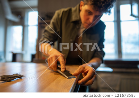 Man woodworker removes splinters from tabletop with chisel, ensuring smooth surface for finishing Man woodworker removes splinters from tabletop with chisel, ensuring smooth surface for finishing 121678583