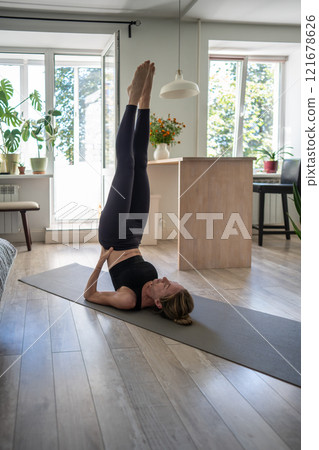 Woman holds shoulder stand pose Sarvangasana, lying on back with legs raised vertically and hands supporting them. Woman holds shoulder stand pose Sarvangasana, lying on back with legs raised vertically and hands supporting them. 121678626