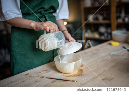 Craftswoman covers handmade ceramic saucer with glaze use jug, ensuring even coat in pottery studio Craftswoman covers handmade ceramic saucer with glaze use jug, ensuring even coat in pottery studio 121678643