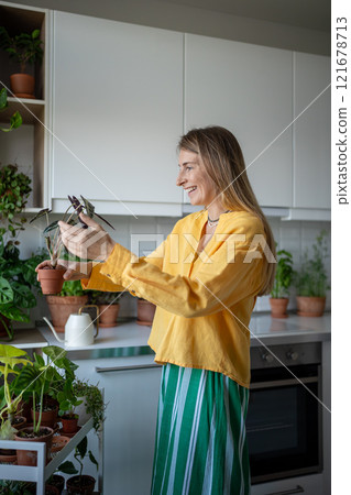 Smiling woman plant lover looks at Alocasia Bambino plant, grown with care at home. Hobby concept 121678713