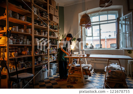 Female potter shaping white clay mug on table in pottery workshop. Prepare mug for drying, firing Female potter shaping white clay mug on table in pottery workshop. Prepare mug for drying, firing 121678755