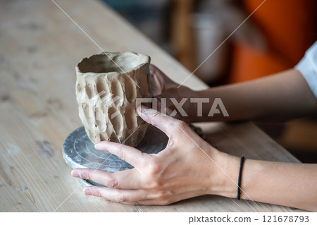 Woman potter hands carefully molding patterned vase or bowl in pottery studio. Textured sculpting 121678793