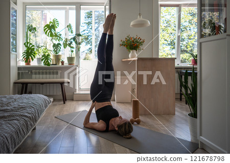 Woman holds shoulder stand pose Sarvangasana, lying on back with legs raised vertically and hands supporting them. Woman holds shoulder stand pose Sarvangasana, lying on back with legs raised vertically and hands supporting them. 121678798