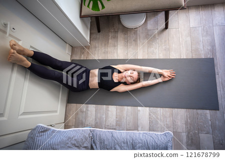 Sportive woman with closed eyes, meditating on mat with feet against door and arms extended overhead 121678799