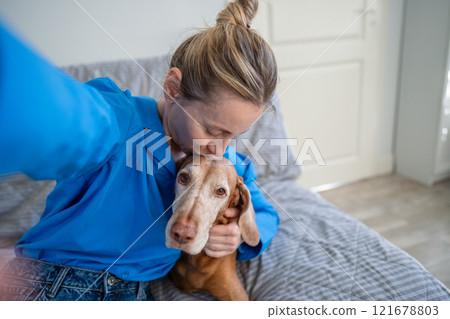 Woman taking selfie, kissing and hugging dog on couch at home. Pet adoption, healthy pet, dog lover 121678803