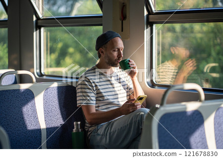 Calm man sip tea from thermos, chatting on smartphone in train car in morning. Male travel pause Calm man sip tea from thermos, chatting on smartphone in train car in morning. Male travel pause 121678830