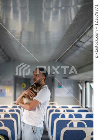 Caring man cradles scared cat on train, easing pet stress during travel. Road trip with nervous pet Caring man cradles scared cat on train, easing pet stress during travel. Road trip with nervous pet 121678871