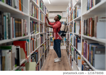 Thoughtful African American student man in glasses choosing book in college library or bookstore 121678898