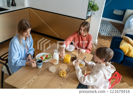 Attentive caring mother with teen daughter and kid son eat before school. Family healthy breakfast Attentive caring mother with teen daughter and kid son eat before school. Family healthy breakfast 121678916