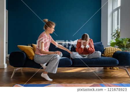 Loving supportive mother comforting upset crying teen daughter while sitting together on sofa 121678923