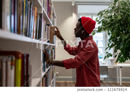 Concentrated black student guy picking literature checking information in library for study project. Concentrated black student guy picking literature checking information in library for study project. 121678924