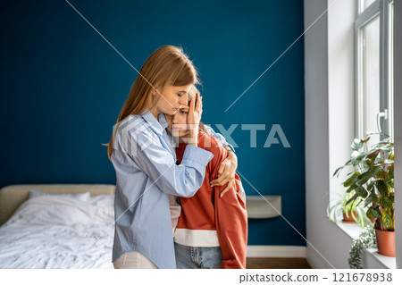 Young caring woman stands at home and hugging teenage girl needing support after school troubles 121678938