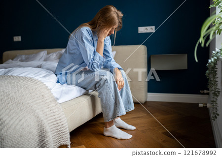 Young unhappy woman sitting on bed at home suffering from headache 121678992