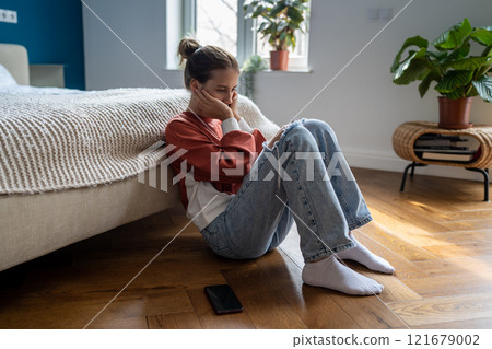 Depressed teenage girl sitting on floor at home with smartphone waiting for call from boyfriend Depressed teenage girl sitting on floor at home with smartphone waiting for call from boyfriend 121679002