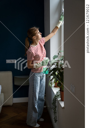 Caucasian woman housewife wearing casual clothes and rubber gloves cleaning window glass in bedroom 121679012