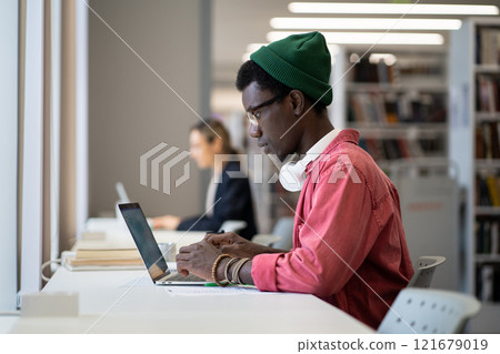 Entrepreneurial independent African American man works sits with laptop in library building Entrepreneurial independent African American man works sits with laptop in library building 121679019