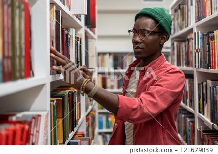 African guy University student standing between bookshelves in library African guy University student standing between bookshelves in library 121679039