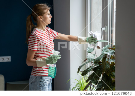 Caucasian woman housewife wearing casual clothes and rubber gloves cleaning window glass in bedroom Caucasian woman housewife wearing casual clothes and rubber gloves cleaning window glass in bedroom 121679043